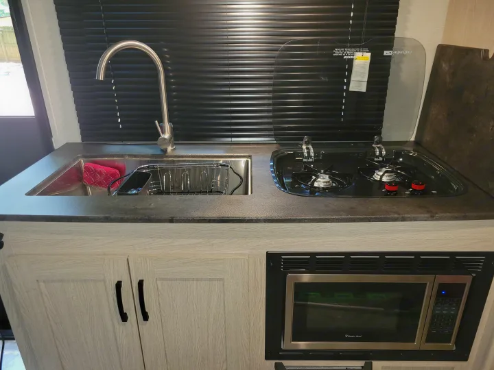 Compact RV rental kitchen features a sink, 2-burner stove with cover, and built-in microwave, ready for your adventures.. Other Other 2022