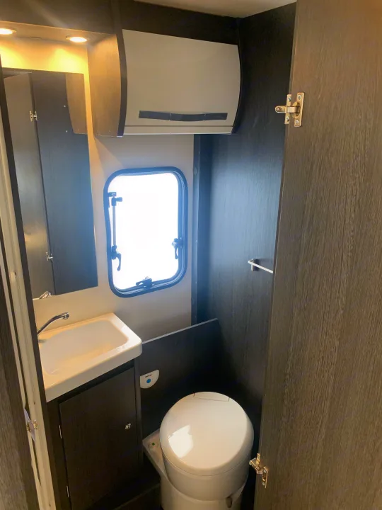 Compact RV rental bathroom with white sink, toilet, small window, and dark wood cabinetry.. Rollerteam Zefiro 675 (Auto) 2022