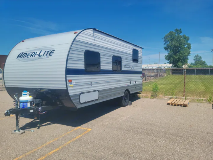 An Ameri-Lite travel trailer, ideal for rv rental, is parked on asphalt under a clear blue sky. It features a visible propane tank.. Gulf Stream Ameri-Lite Super Lite 2021