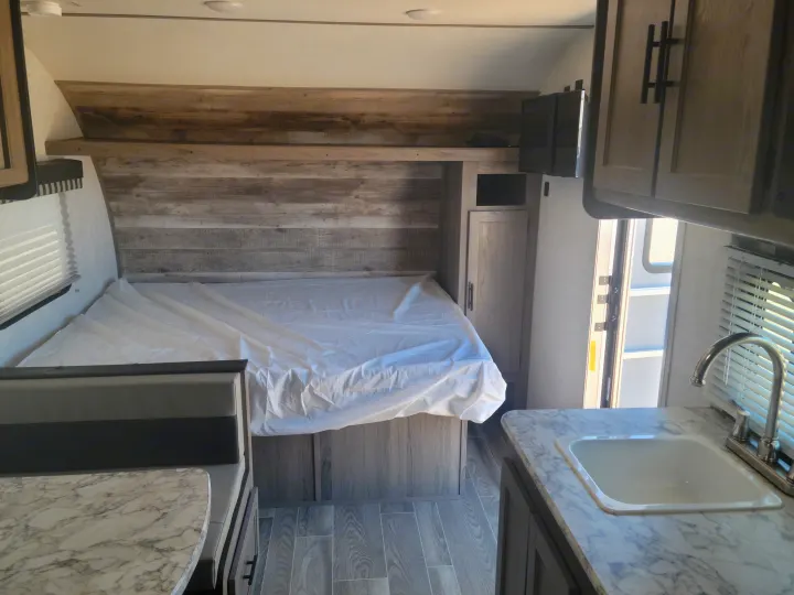 Inside a modern RV rental: view of bed area, dinette with table, and compact kitchen with sink. Perfect for trips!. Gulf Stream Ameri-Lite Super Lite 2021
