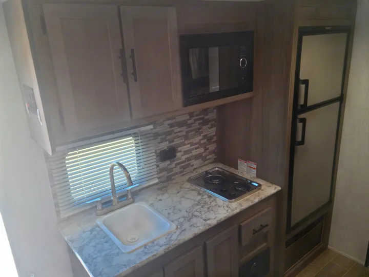 Compact RV rental kitchen with sink, microwave, two-burner stove, and refrigerator for convenient travel.. Gulf Stream Ameri-Lite Super Lite 2021