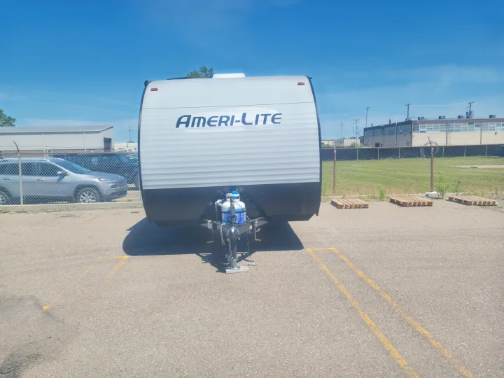 An Ameri-Lite travel trailer, propane tanks visible, parked on asphalt. Ideal for rv rental adventures.. Gulf Stream Ameri-Lite Super Lite 2021