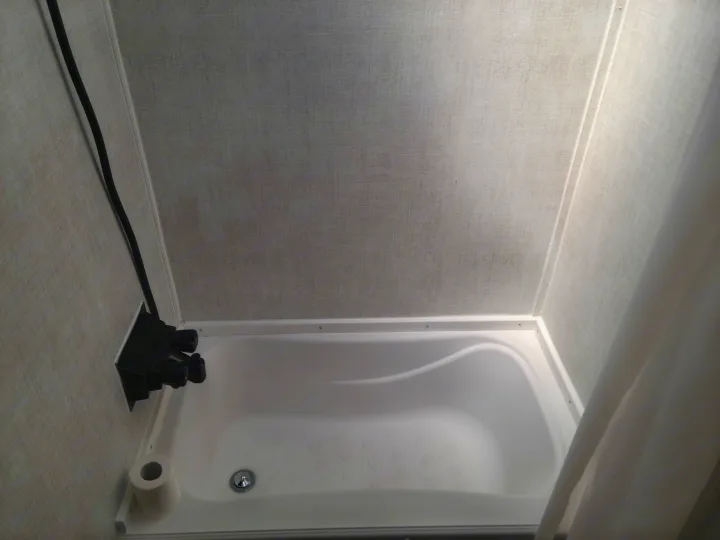 Compact RV rental shower featuring a white tub with non-slip floor, black controls, and textured walls.. Gulf Stream Ameri-Lite Super Lite 2021