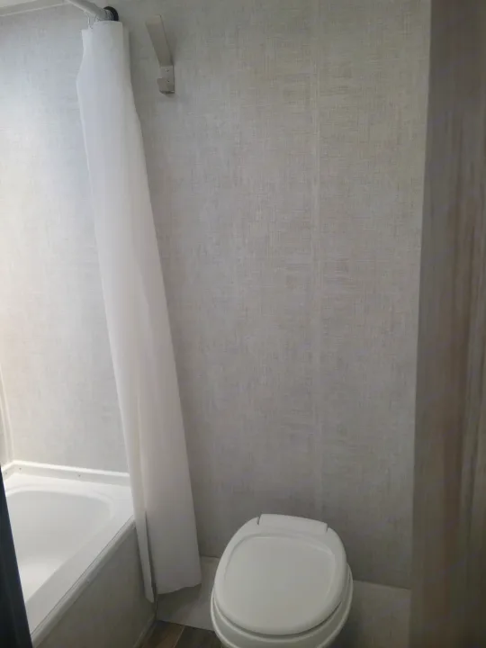 Inside an RV rental, this bright bathroom features a tub, toilet, and white shower curtain.. Gulf Stream Ameri-Lite Super Lite 2021