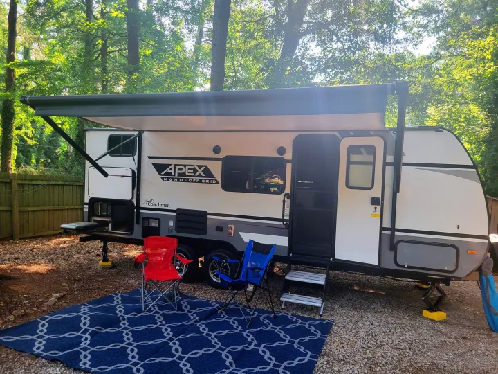 A clean RV rental camper with an extended awning, outdoor kitchen, and chairs on a blue rug at a serene campsite.. Other Other 2022
