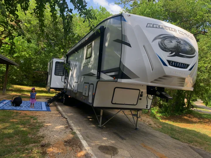 Family camping with an Arctic Wolf Cherokee fifth-wheel RV rental, parked at a treed site with a child and mat.. Forest River Cherokee Arctic Wolf 2022