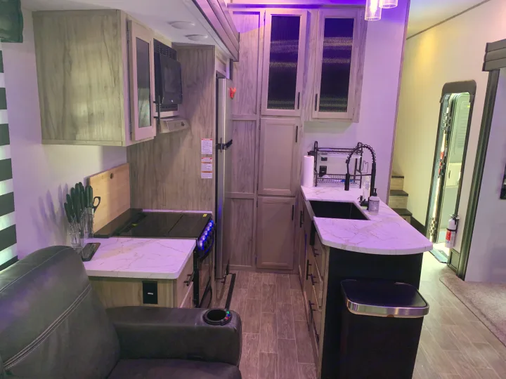 Modern RV rental interior with a well-equipped kitchen, sofa seating, and appliances, bathed in a soft purple light.. Forest River Cherokee Arctic Wolf 2022
