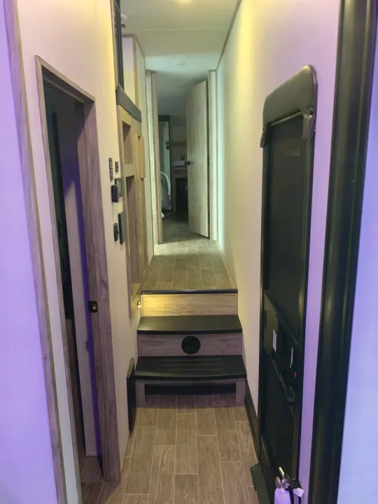 Cozy RV rental interior: A modern hallway with steps leading down to a bedroom, highlighting a functional living space.. Forest River Cherokee Arctic Wolf 2022