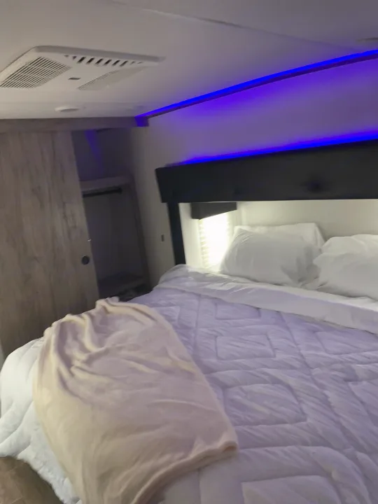 Cozy RV rental bedroom featuring a comfy bed, blue LED lights, a closet, and ceiling AC vent for comfort.. Forest River Cherokee Arctic Wolf 2022