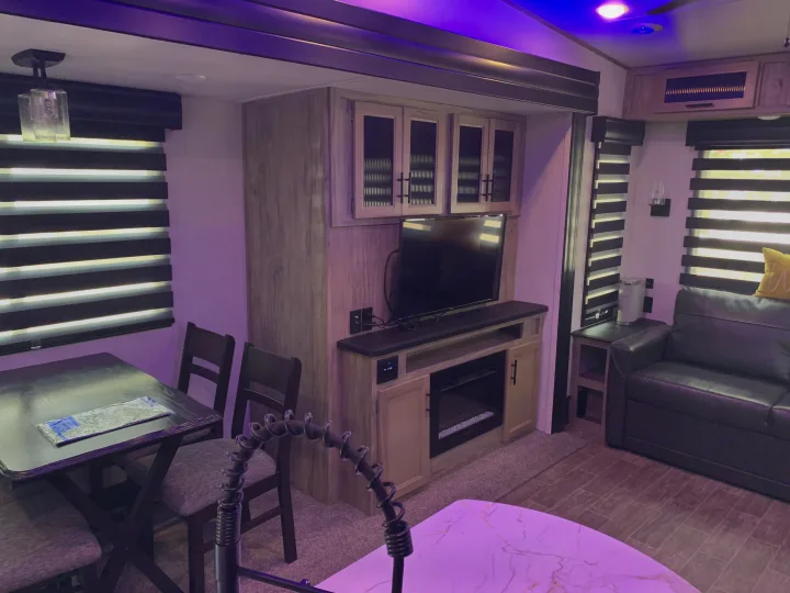 Cozy RV rental interior featuring a dining area, entertainment center with TV & fireplace, and a sofa. Accented by purple lighting.. Forest River Cherokee Arctic Wolf 2022