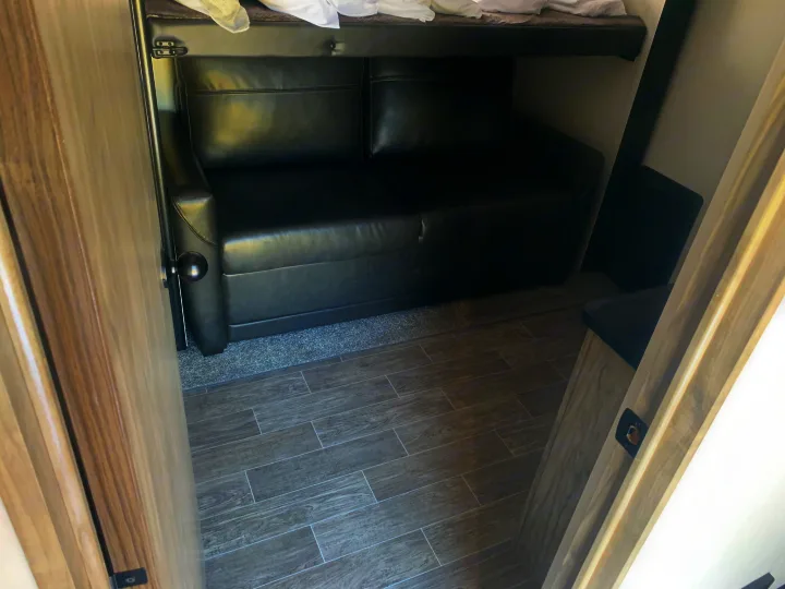 RV rental interior view shows a black sofa under a bunk bed and stylish wood-look flooring, offering compact living space.. Forest River Cherokee Arctic Wolf 2022