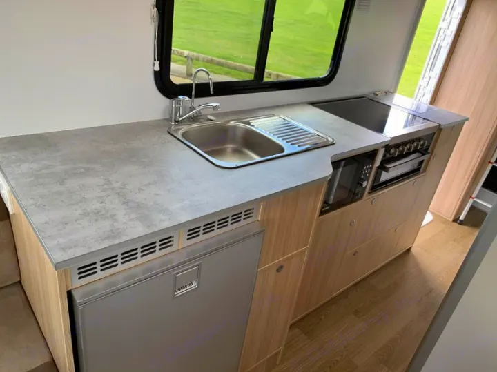An RV rental's well-equipped kitchen featuring a sink, cooktop, microwave, and fridge for on-the-go living.. Mercedes-Benz Sprinter 2022