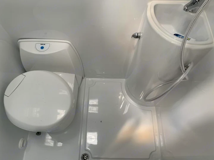 This RV rental's compact wet bath features a toilet, corner sink, and shower head for efficient travel.. Mercedes-Benz Sprinter 2022