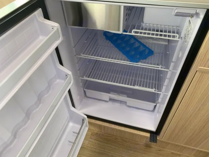 Empty, clean RV rental refrigerator interior with wire shelves, freezer, and blue ice tray. Ready for your adventure.. Mercedes-Benz Sprinter 2022