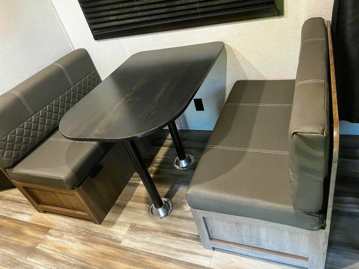 Modern RV rental dinette featuring dark upholstered bench seats with white stitching & a table on wood-look flooring.. Open Range Open Range 2022