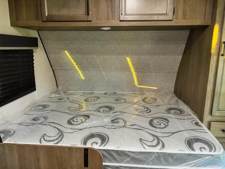 RV rental bedroom featuring a new mattress still in plastic wrap, overhead cabinets, and a compact design.. Open Range Open Range 2022
