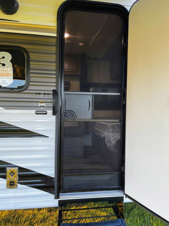 RV rental: Open screen door of a travel trailer, revealing the interior living space and exterior steps.. Open Range Open Range 2022
