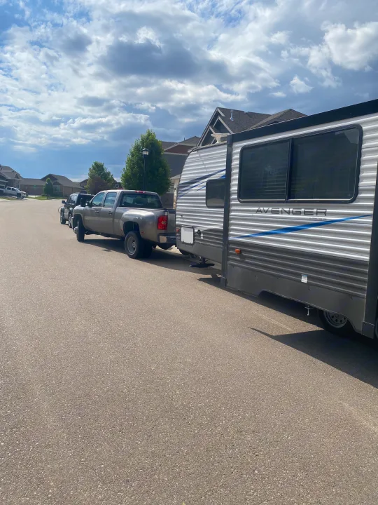 Gray pickup truck towing an Avenger travel trailer, perfect for your next RV rental adventure, parked on a residential street.. Prime Time Avenger 2021