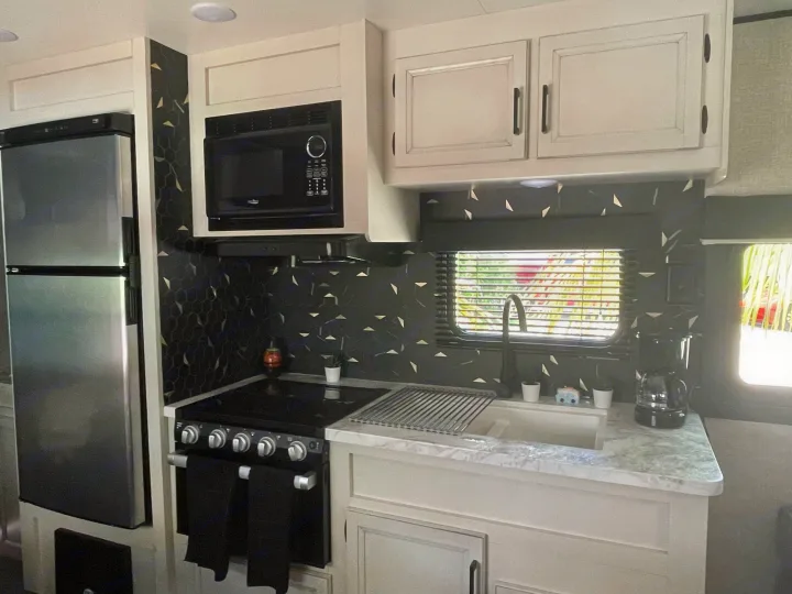 Compact RV rental kitchen featuring a fridge, microwave, stove, and sink with a modern dark and gold backsplash.. Jayco JAYCO JAY FLIGHT SLX 264BH 2022