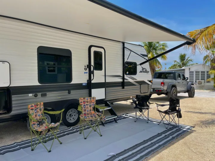 Sunny RV rental campsite setup: white travel trailer with awning, silver Jeep Gladiator, chairs, and outdoor mat.. Jayco JAYCO JAY FLIGHT SLX 264BH 2022