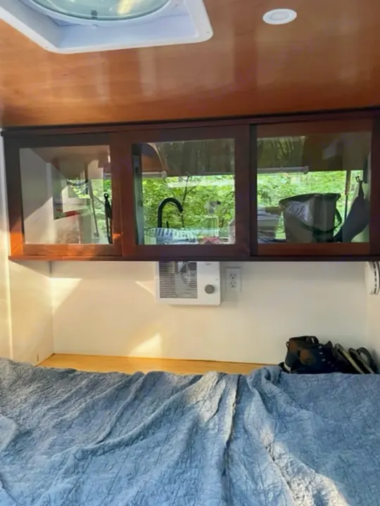 RV rental interior: wood cabinets with a sink view, wall heater, and a blue-quilted bed.. Driftwood Trailers Other 2022