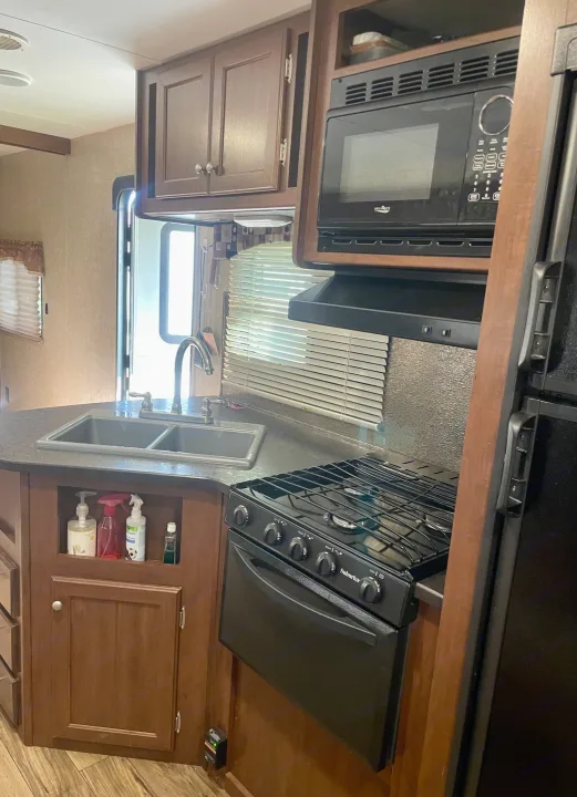 Compact RV kitchen with a double sink, microwave, stove/oven, and storage. Ideal for any rv rental adventure.. Heartland RVs Pioneer 2016
