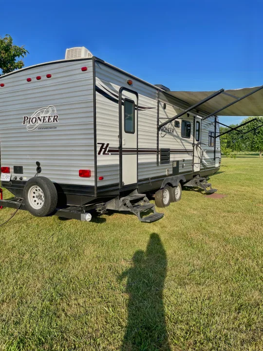 Grey Pioneer travel trailer parked on grass with awning extended under a clear sky, ready for an RV rental adventure.. Heartland RVs Pioneer 2016