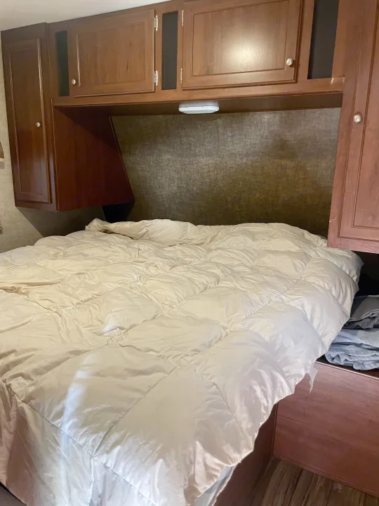Cozy RV rental bedroom with a comfortable bed and light comforter, dark wood overhead cabinets, and built-in side storage.. Heartland RVs Pioneer 2016