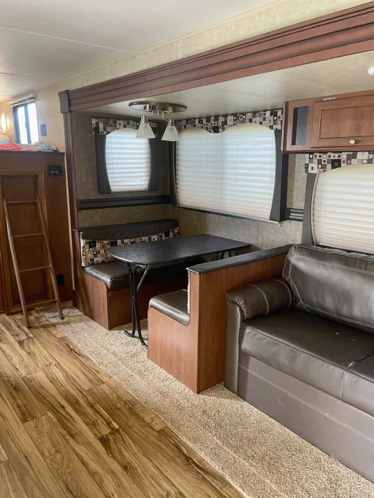 Inside an RV rental: a comfortable living area with a dining booth, sofa, and ladder to a bunk, showcasing the roomy interior.. Heartland RVs Pioneer 2016
