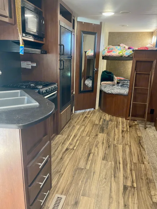 RV rental interior shows kitchen with sink, stove, microwave, fridge, and bunk beds in a cozy space.. Heartland RVs Pioneer 2016