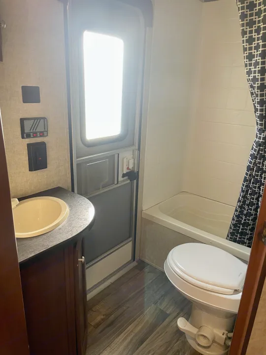 This RV rental features a functional bathroom with a compact sink, toilet, and bathtub/shower setup, plus wall controls.. Heartland RVs Pioneer 2016