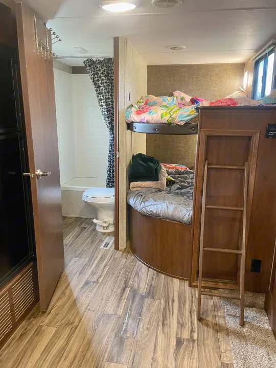Inside an RV rental: bunk beds, a full bathroom with toilet/shower, and wood-look flooring. Perfect for family trips!. Heartland RVs Pioneer 2016
