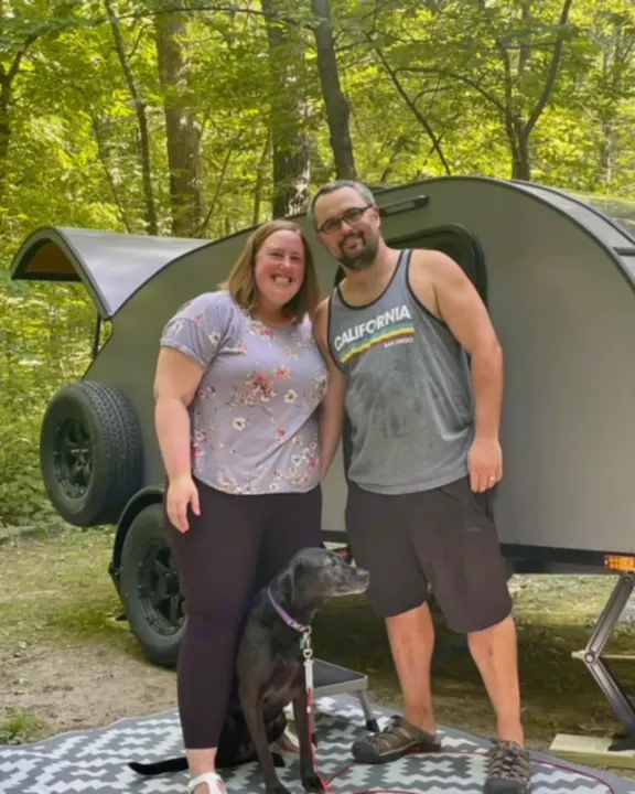 Happy couple & dog enjoying their RV rental, a gray teardrop trailer, at a shady campsite. Perfect camping trip!. Driftwood Trailers Other 2022
