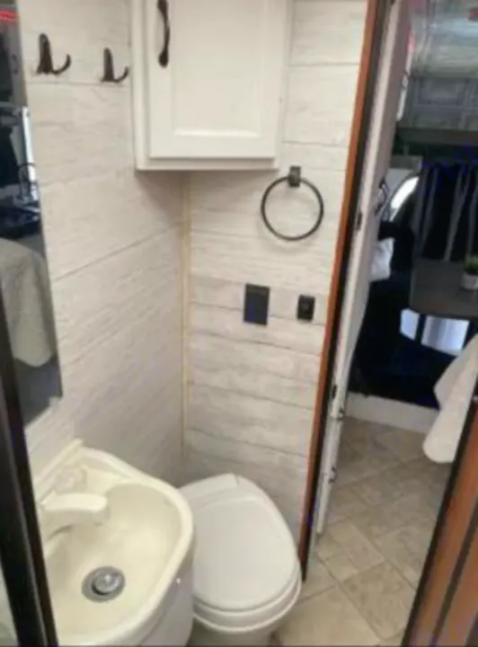 Compact RV rental bathroom with white shiplap walls, sink, toilet, cabinet, hooks, and towel ring.. Forest River Coachmen Freelander 2010