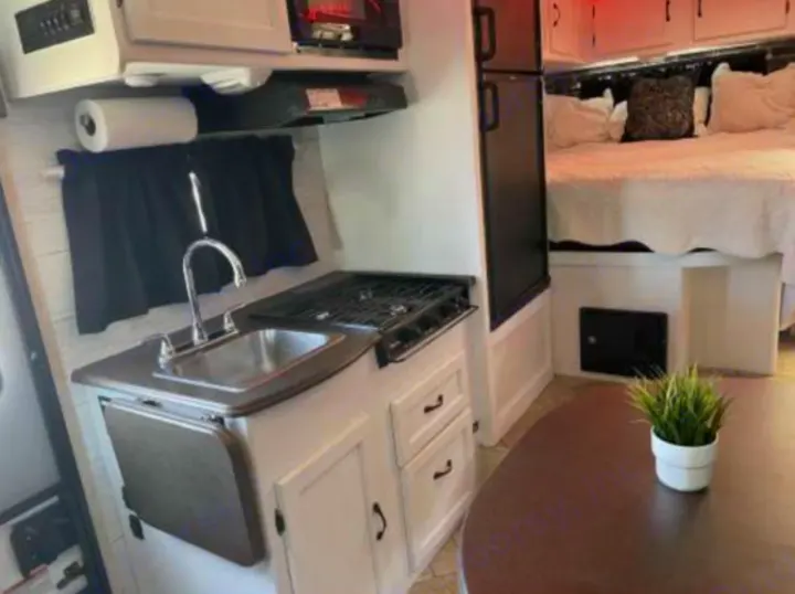 Well-equipped RV rental interior featuring a compact kitchen with stove, sink, bedroom, and dining area.. Forest River Coachmen Freelander 2010
