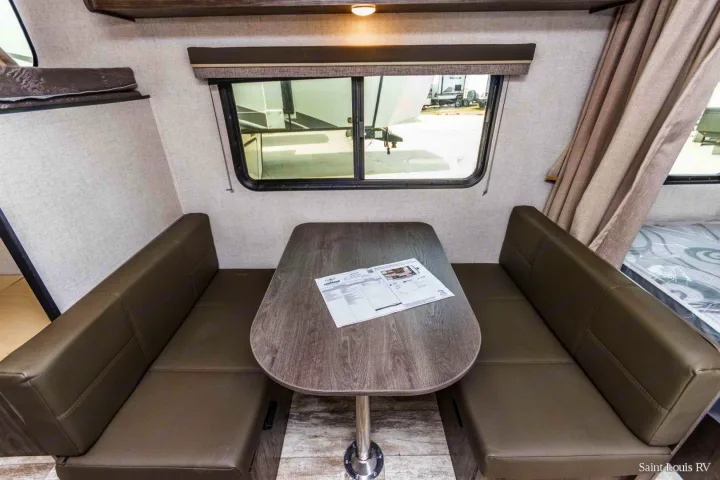 This RV rental interior features a dinette with a wood-grain table and two gray upholstered benches, beside a large window.. Highland Ridge RV Open Range 2020