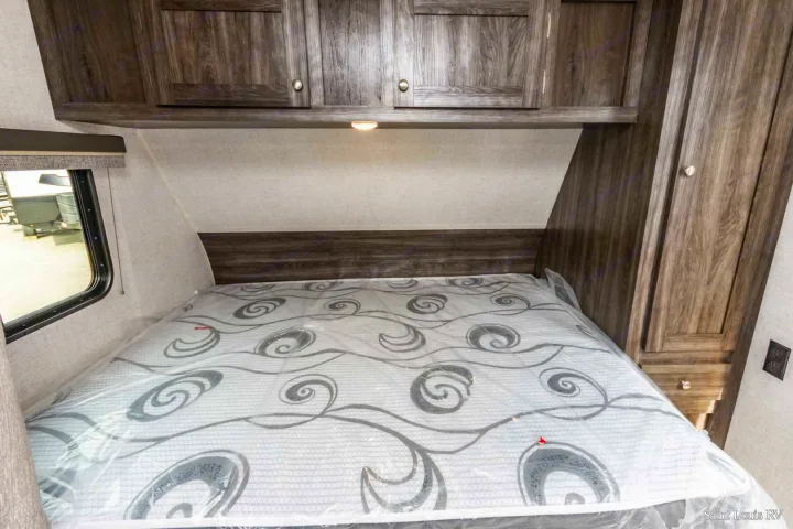 Compact RV rental bedroom with dark wood cabinets above bed, a window, and a mattress still in plastic wrap. Perfect for travel.. Highland Ridge RV Open Range 2020