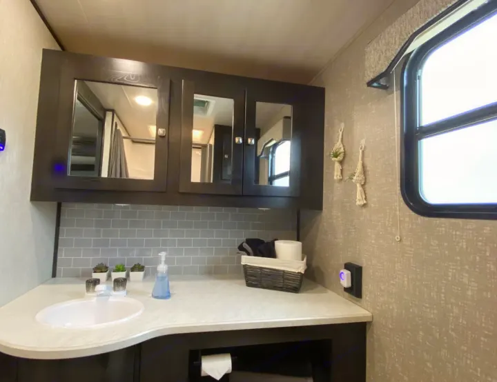 Modern RV rental bathroom with dark cabinets, sleek sink, gray subway tile backsplash, and a window. Neatly organized space.. Heartland RVs North Trail 2019