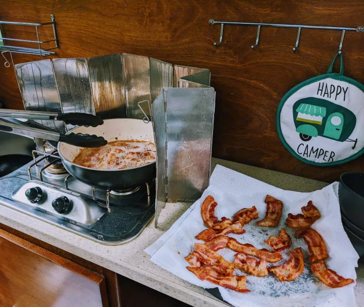 Frying bacon in an RV rental kitchen, with a wind guard and a "Happy Camper" pot holder. Perfect camper cooking!. T@G XL 2016