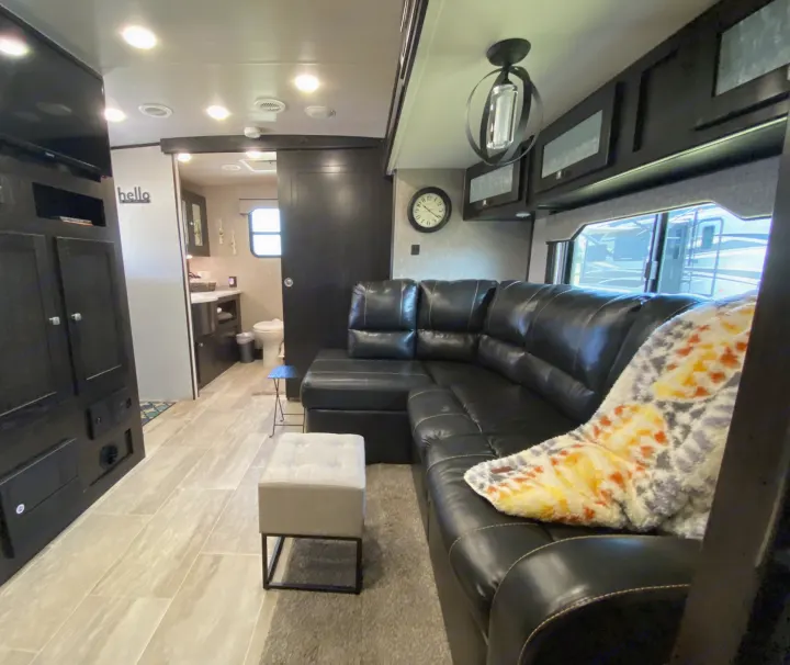 Modern RV rental living space featuring a black sectional couch, smart TV, stylish decor, and access to a full bathroom.. Heartland RVs North Trail 2019