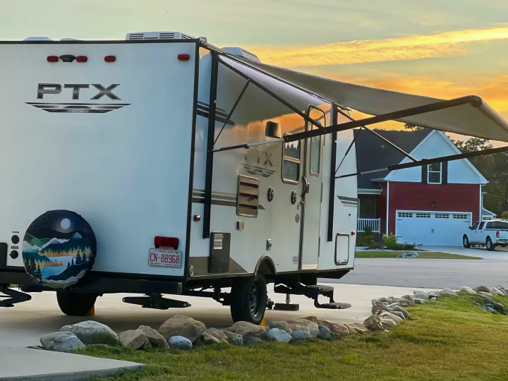 A PTX travel trailer, ideal for an RV rental, is parked with its extended awning, reflecting the soft sunset glow.. PTX Forest River PDX170 2019