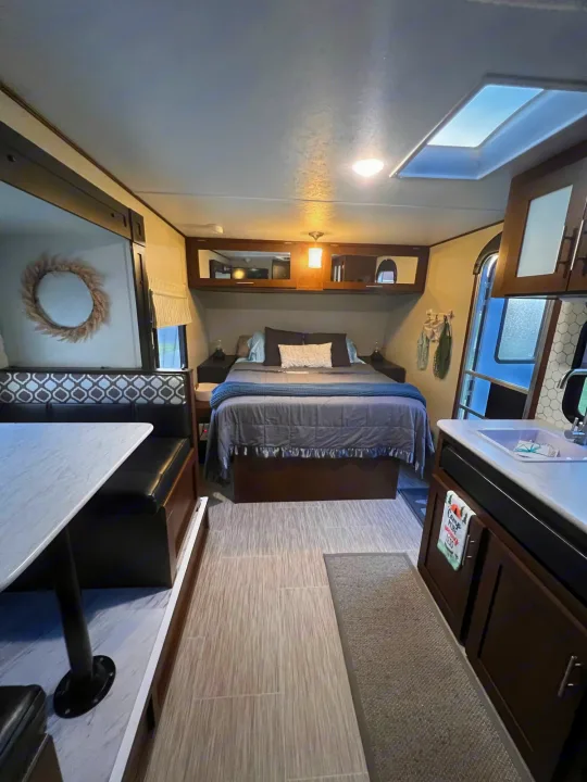 Cozy RV rental interior with a comfortable bed, dinette, kitchen, and skylight – your home on wheels.. PTX Forest River PDX170 2019