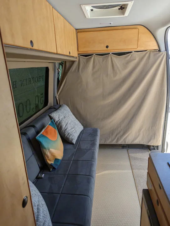 Spacious RV rental interior: overhead wooden cabinets, sofa with pillows, privacy curtain, and modern flooring for comfortable travel.. Freightliner Sprinter Van 2012