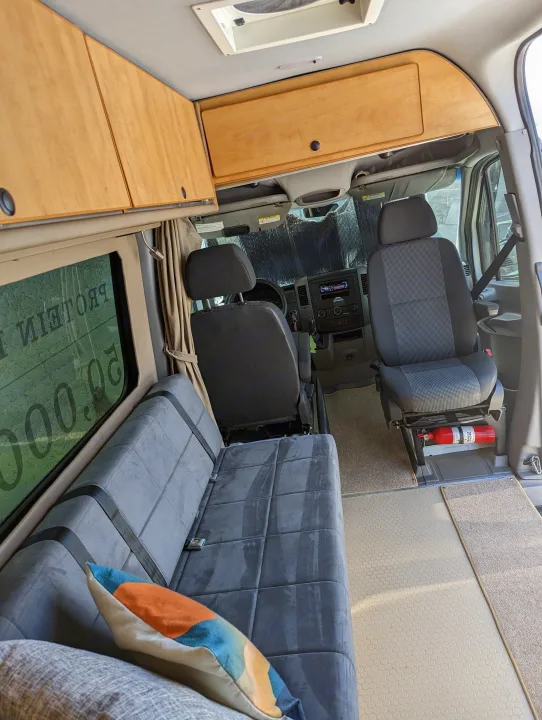 Step inside this RV rental camper van, featuring a multi-person bench, wooden cabinets, and front seating area.. Freightliner Sprinter Van 2012