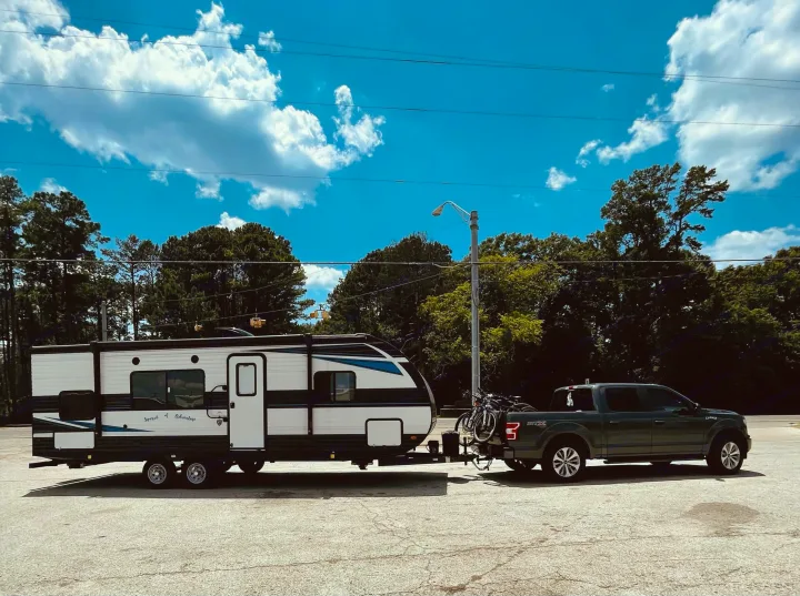 Green pickup truck tows a white RV and bikes, ready for adventure. Explore RV rental options for your journey!. Heartland Prowler 2021
