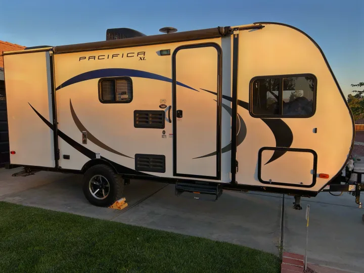 This clean, white Pacifica XL travel trailer RV rental with an awning is parked on a driveway next to grass.. Pacific Coachworks Pacifica XL 2020