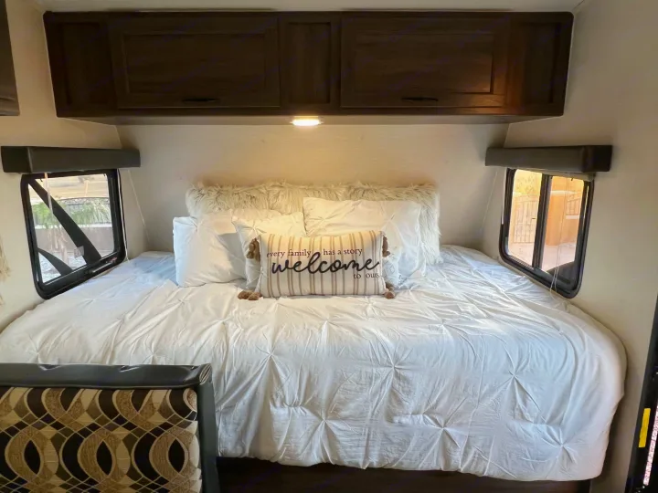 Spacious & cozy RV bedroom features a large white bed, inviting pillows, overhead cabinets, and side windows. Ideal for RV rental.. Pacific Coachworks Pacifica XL 2020