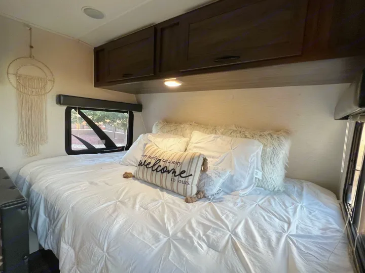 Discover a cozy RV rental bedroom featuring a large bed with white linens, a welcome pillow, and storage cabinets.. Pacific Coachworks Pacifica XL 2020