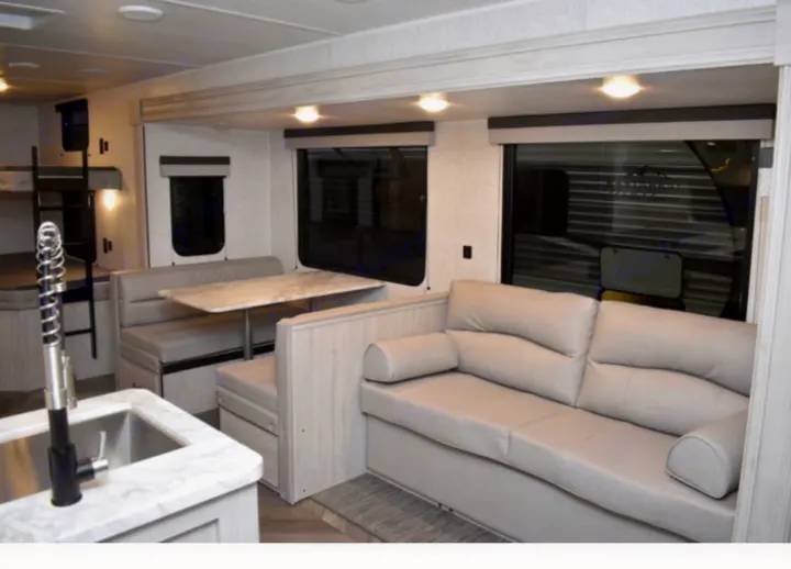 Spacious RV rental interior featuring a dinette, comfy sofa, kitchen sink, and bunk beds. Ideal for family adventures!. East to West Other 2022
