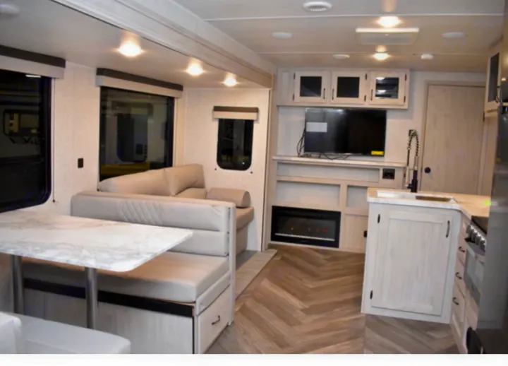 Inside a bright RV rental: modern living area with dinette, sofa, fireplace, and kitchen. Perfect for trips.. East to West Other 2022